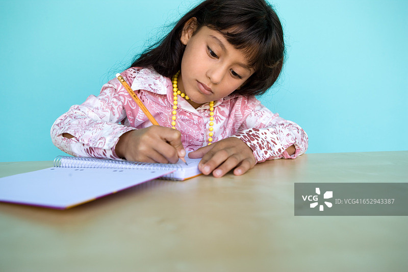 一个小女孩在她的笔记本上写字。图片素材