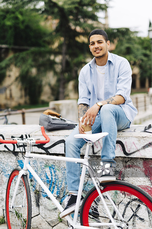 微笑的年轻人骑着自行车坐在涂鸦墙上图片素材