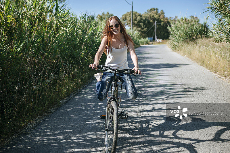 快乐的年轻女子骑自行车在乡村小路上图片素材