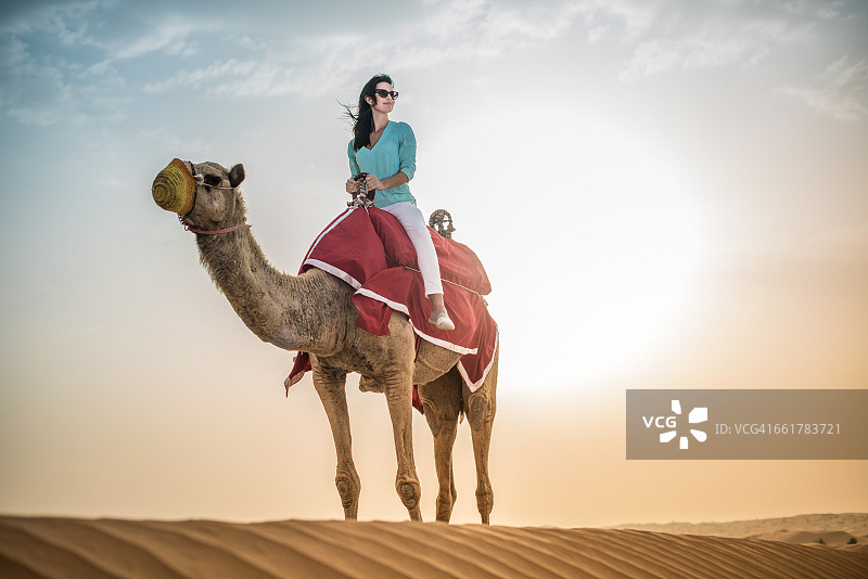 阿拉伯联合酋长国迪拜沙漠中骑骆驼的女游客图片素材