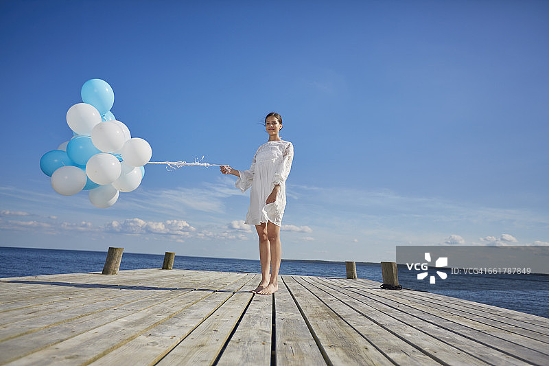 年轻女子的肖像，站在木码头，拿着一束气球图片素材