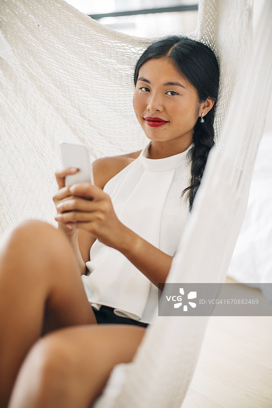 一个年轻女子在吊床上拿着手机图片素材