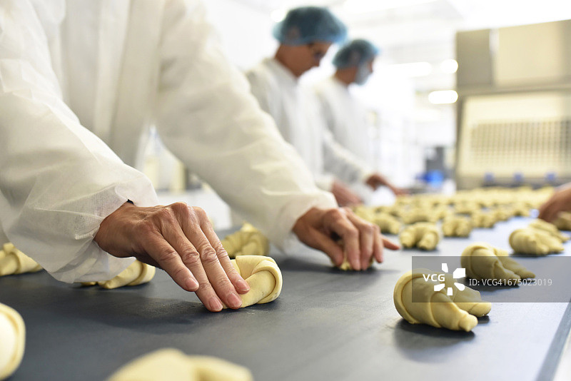 在一家制作牛角面包的烘焙工厂生产线上的工人们图片素材