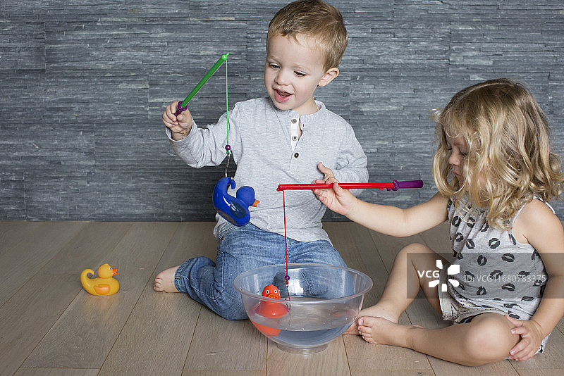 孩子们用玩具鱼竿钓起漂浮在大碗里的橡皮鸭图片素材