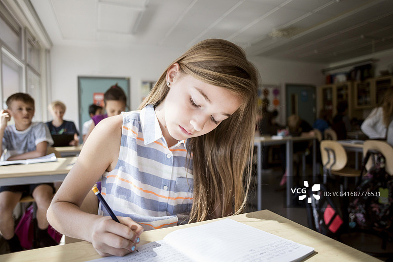 女孩在桌子上写书，学生坐在后面图片素材