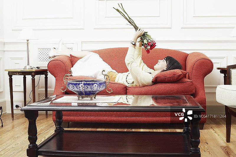 一个年轻女子的侧影躺在沙发上，手里拿着一束花图片素材