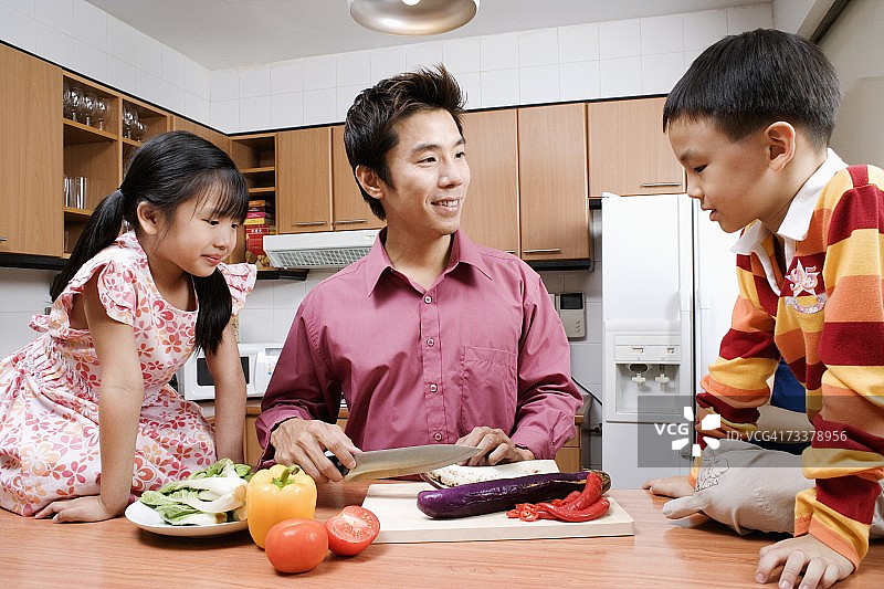 中年男子和他的孩子们在厨房的柜台前切蔬菜图片素材