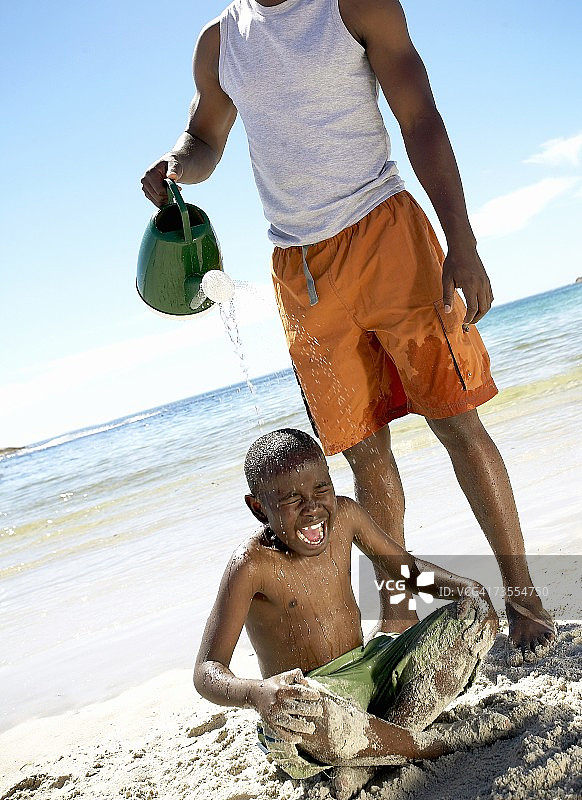 非洲男子将水浇在儿子的头上图片素材