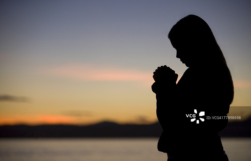 一个十几岁的女孩在海边的日落祈祷。图片素材