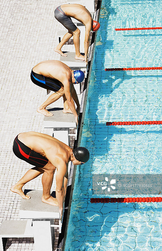 三个游泳运动员在泳池起跑线上图片素材