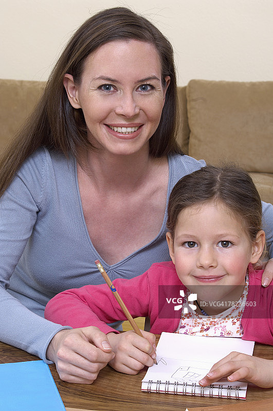 母亲帮助小女儿做家庭作业的肖像图片素材