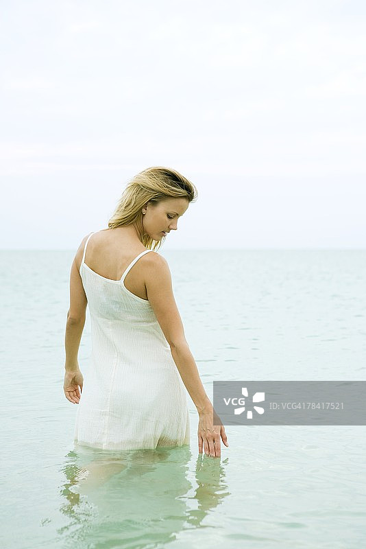 女人站在齐膝深的海洋里，触摸着水面图片素材