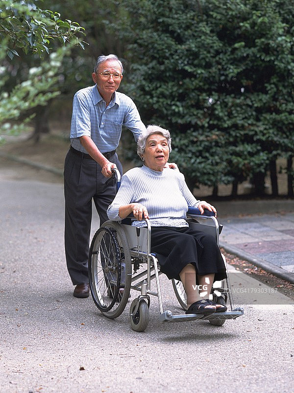 老年妇女的肖像在轮椅上和她的丈夫推它，前视图图片素材