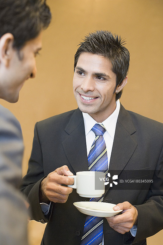 一个商人拿着一杯茶和他的同事交谈的特写图片素材