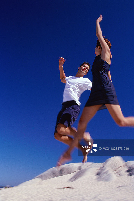 年轻夫妇在海滩上跳跃，低角度视角(模糊动作)图片素材