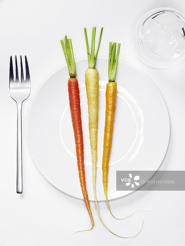 三个不同颜色的胡萝卜放在一个白色的盘子里。图片素材
