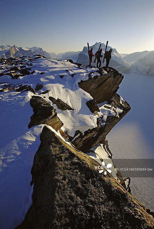 加拿大巴芬岛，三个滑雪者站在悬崖边望着冰冻的海洋图片素材