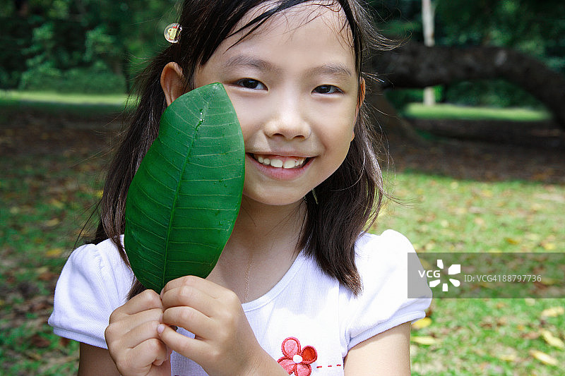一个女孩的肖像，拿着一片树叶，微笑着图片素材