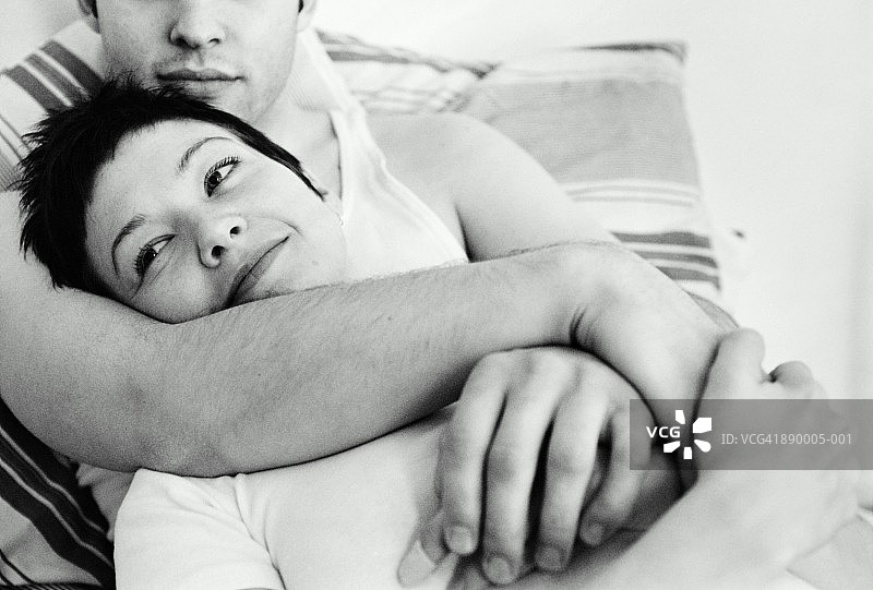 夫妻在床上拥抱，男人的手臂环绕着女人(B&W)图片素材