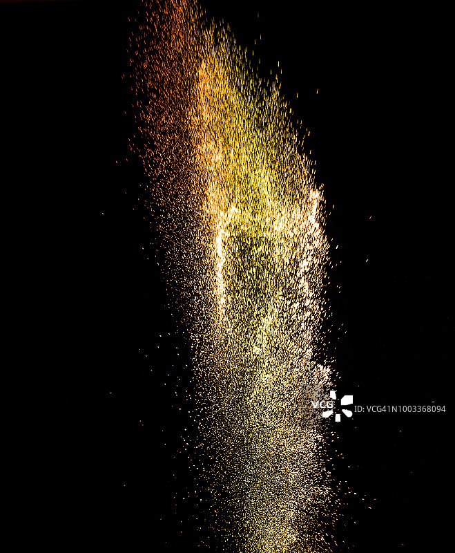 一团红色和黄色的粉末颗粒在黑色的背景上受到冲击而爆炸。图片素材