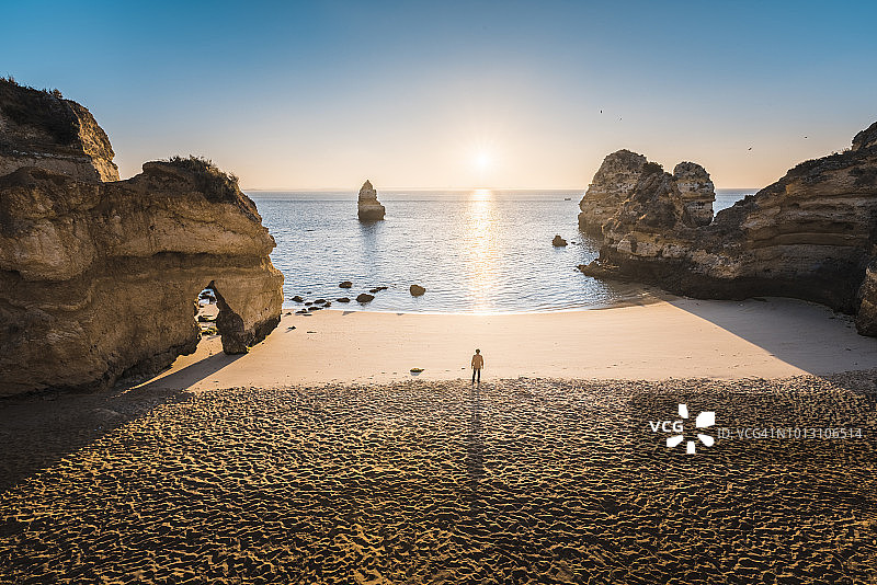 日出时，一个人站在海滩上。高角度的观点。阿尔加维,葡萄牙。图片素材