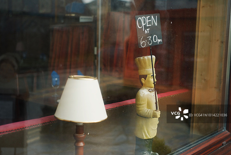 小厨师雕像举着开放的标志在餐厅的窗口图片素材