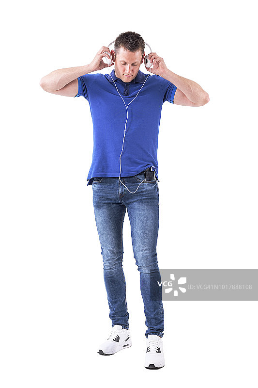 年轻的成年男子放松地戴上耳机，把手机放在口袋里低头看图片素材