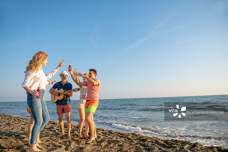 一群快乐的年轻人在美丽的夏日日落的海滩上跳舞图片素材