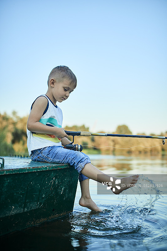 小男孩拿着鱼竿坐在船上溅水图片素材