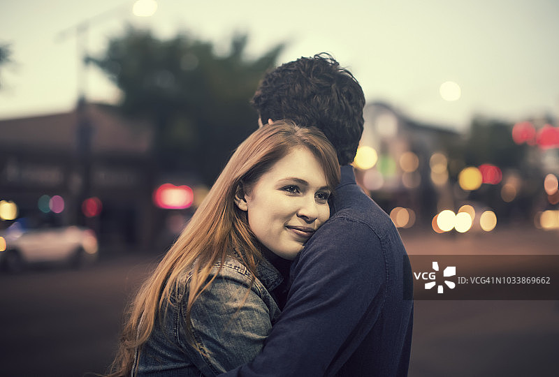 黄昏时分，一对年轻情侣在人流密集的人行道上拥吻图片素材