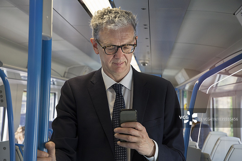 商人站在火车上，看着手机。图片素材