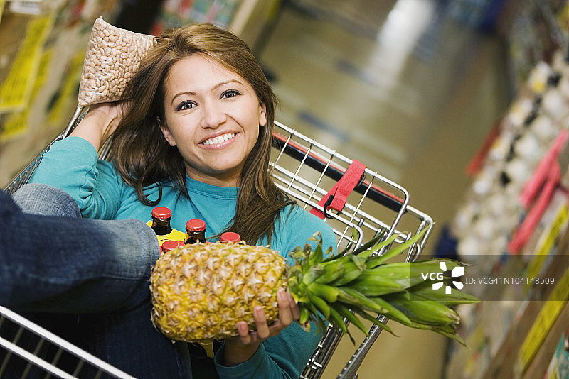 一个年轻女子坐在购物车里，手里拿着一个菠萝图片素材