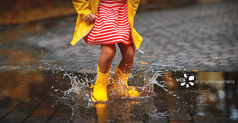 穿着胶靴的孩子的腿在秋天的水坑里行走图片素材