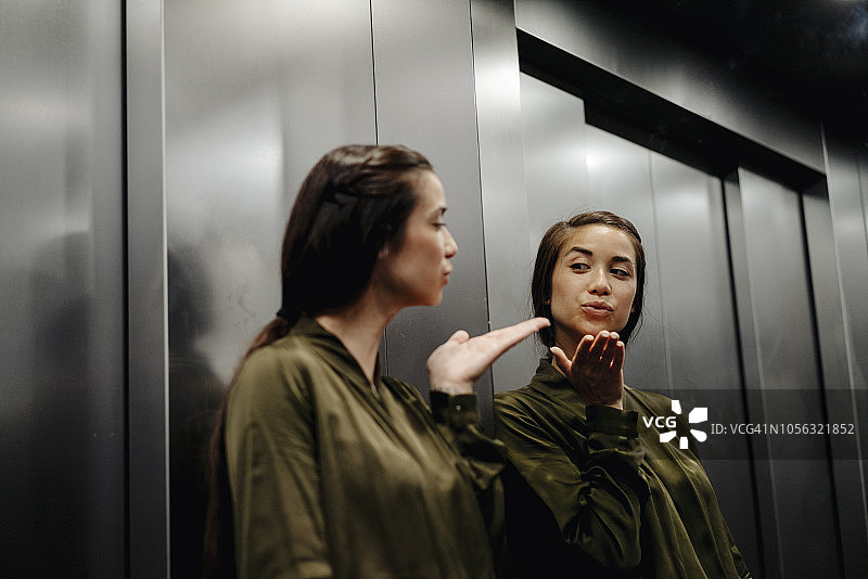 一个年轻女人在电梯里对着镜子飞吻图片素材