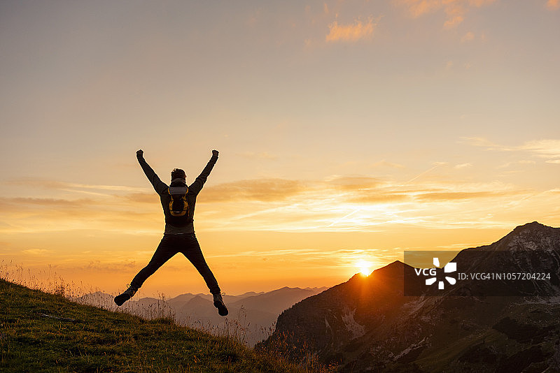 德国，巴伐利亚，奥伯斯多夫，一个男人在日落时在山上徒步跳跃图片素材