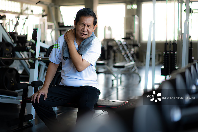 亚洲老年人在健身房锻炼时肩膀疼痛。图片素材