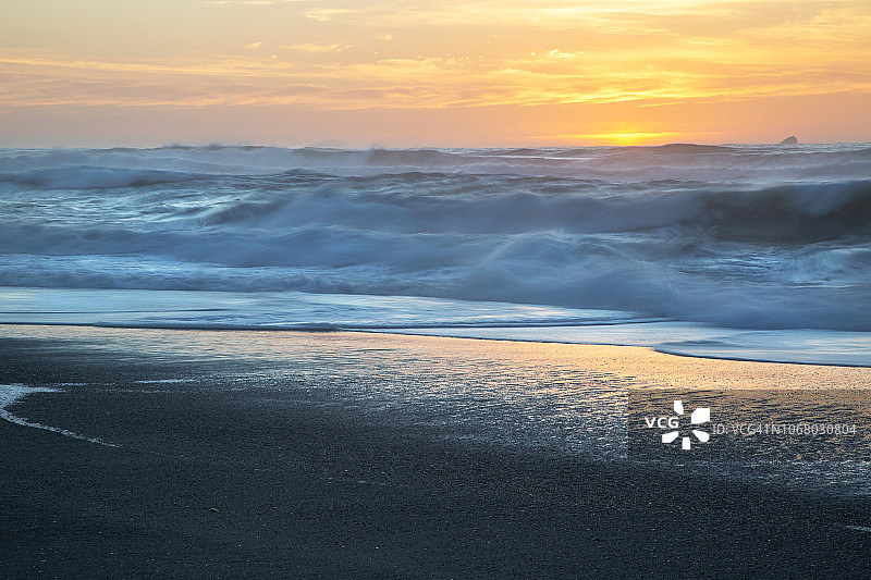 宽阔的镜头抽象模糊的海浪撞击海滩在黎明。图片素材