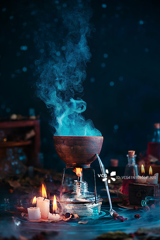 在坩埚里冒着热气的魔法药水。女巫或巫师的工作场所与蜡烛火焰和神秘的项目在一个黑暗的背景与复制空间。图片素材