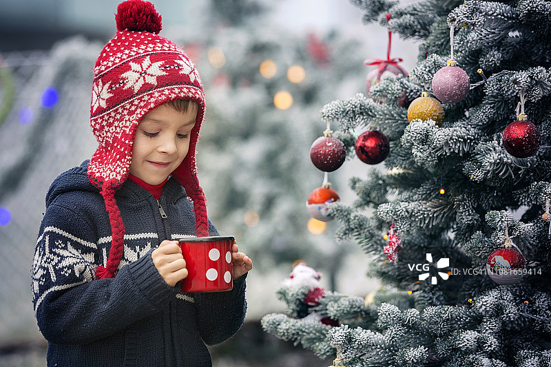 微笑的小男孩喝着热茶，在冬天的森林里装饰圣诞树图片素材