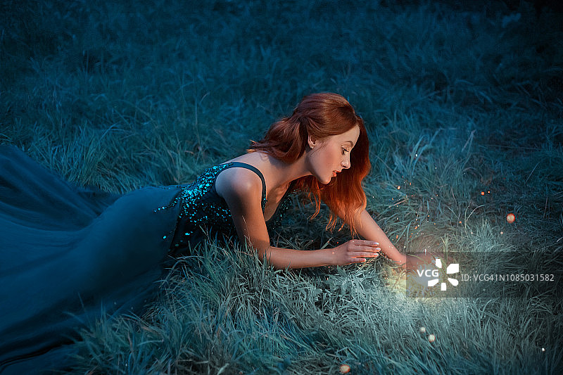 红头发的年轻女子躺在草地上，穿着一件漂亮的拖地长裙图片素材