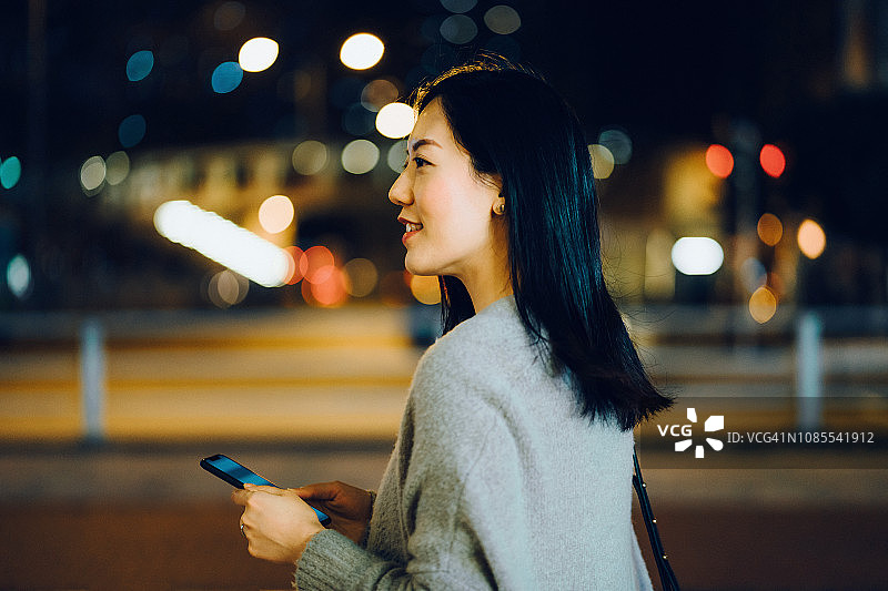 年轻的亚洲女性晚上在商业区使用智能手机图片素材