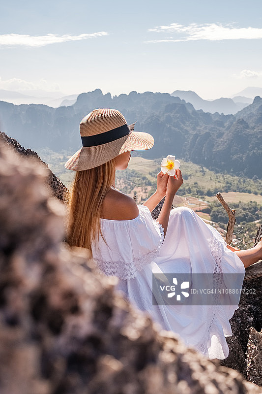 在一个阳光明媚的日子里，一名身穿白色连衣裙的女子站在亚洲的一座山峰上图片素材