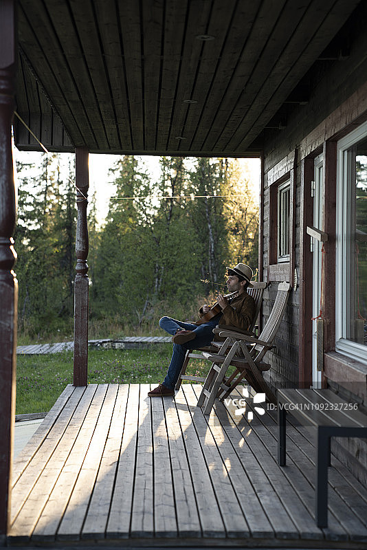 一个年轻人坐在木屋的阳台上，弹着四弦琴图片素材