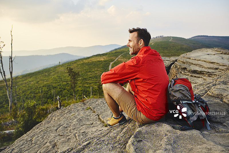 一名男子在徒步旅行中坐在岩石上欣赏风景图片素材