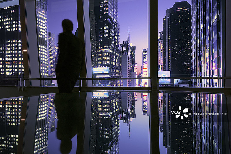 一名男子透过窗户望向纽约时代广场灯火通明的天际线图片素材
