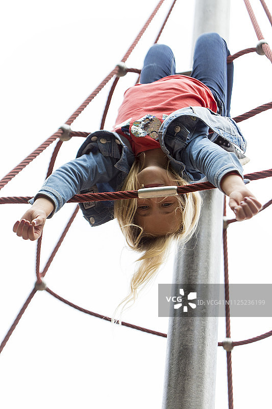 金发女孩倒挂在游乐场的方格架上图片素材