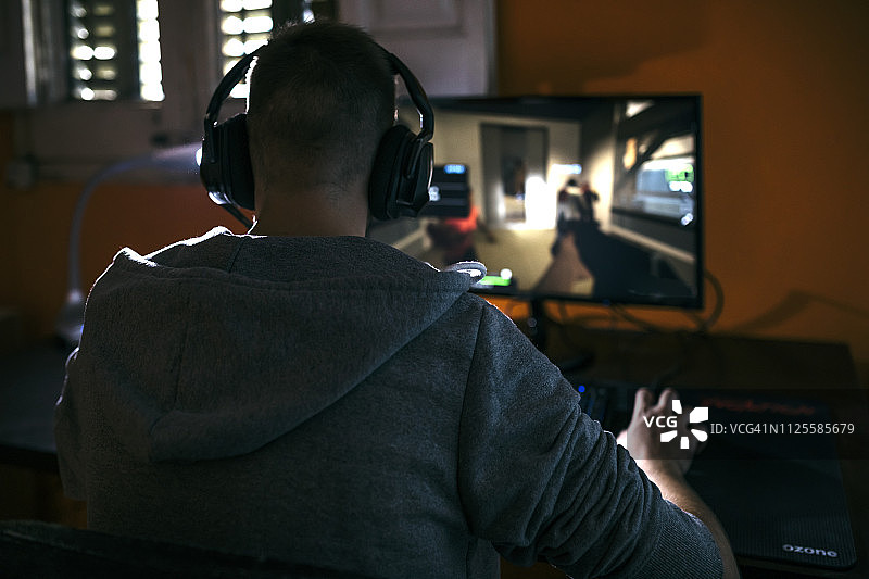 一个年轻人坐在他的电脑前玩电脑游戏图片素材