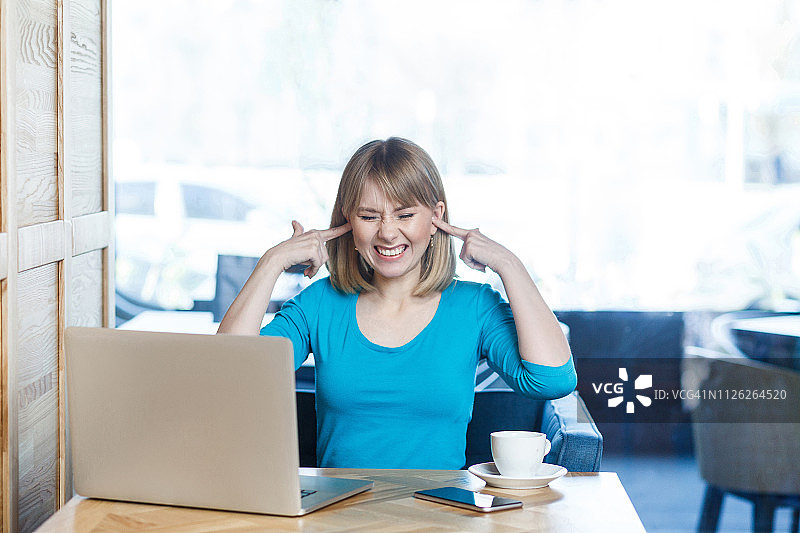 我不想听!肖像吸引有趣的年轻女孩自由职业者在蓝色衬衫坐在咖啡馆，并在笔记本电脑上进行视频通话图片素材
