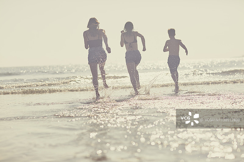 在夏日家庭海滩旅行中，一家人欣喜若狂地跑过大海图片素材