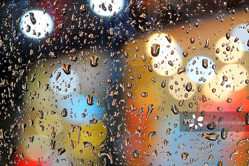 雨滴落在窗户玻璃上，使背景中的彩色灯光散焦图片素材
